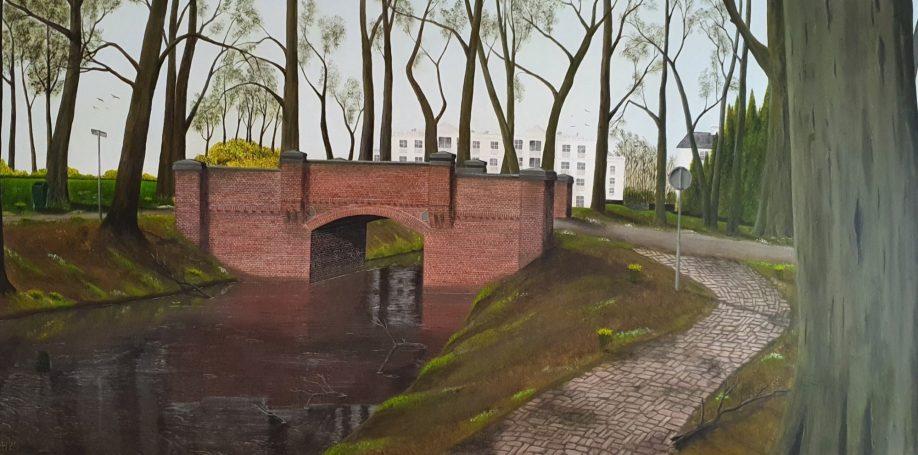 Een brug over een rustige waterloop, omringd door bomen en een pad.
