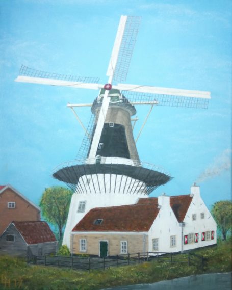 Traditionele Nederlandse molen met huizen en groene bomen onder een blauwe lucht.